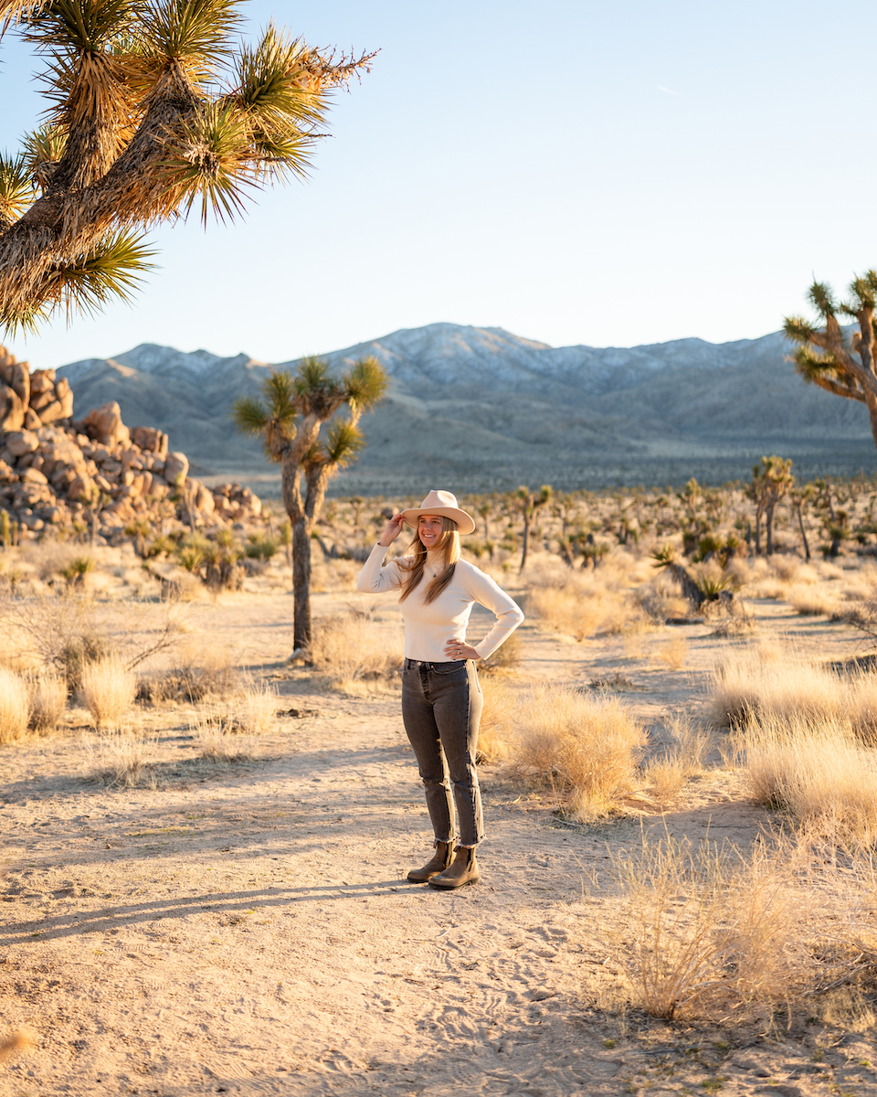 Kate Zittergruen standing on a rocky path with mountains in the distance and trees at Joshua Tree National Park